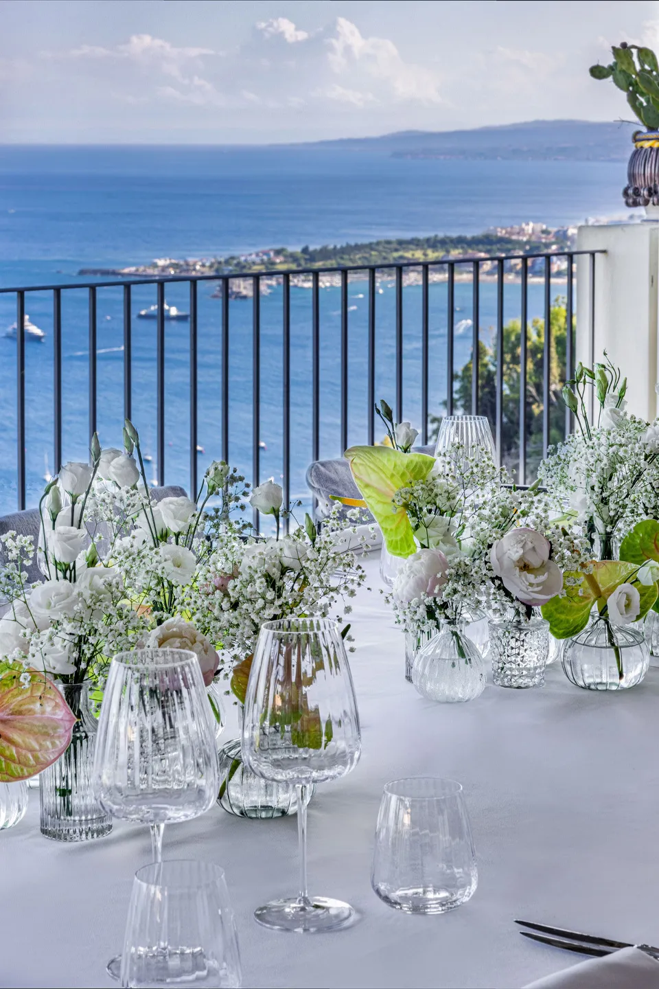 Tavolo apparecchiato del Bellevue Restaurant Hotel Metropole Taormina: fiori bianchi, calici in cristallo e vista sul mare Ionio