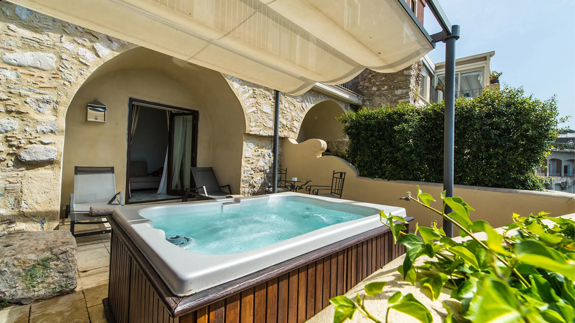 Private terrace with jacuzzi of the Deluxe Pool Room, stone arches and Mediterranean greenery