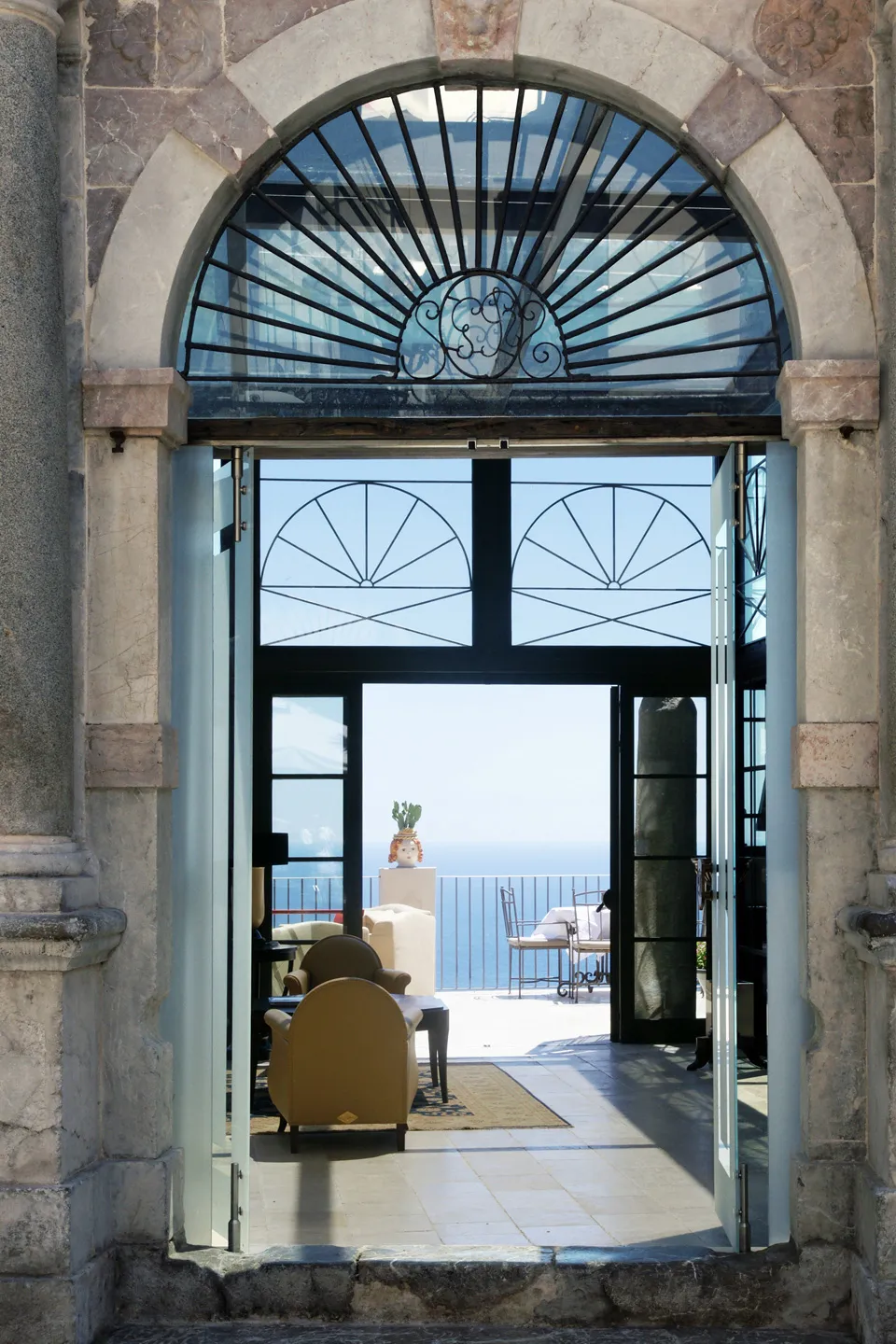 Ingresso principale Hotel Metropole Taormina: portale in pietra con vetrate Liberty, poltrona vintage e vista sul mare Ionio