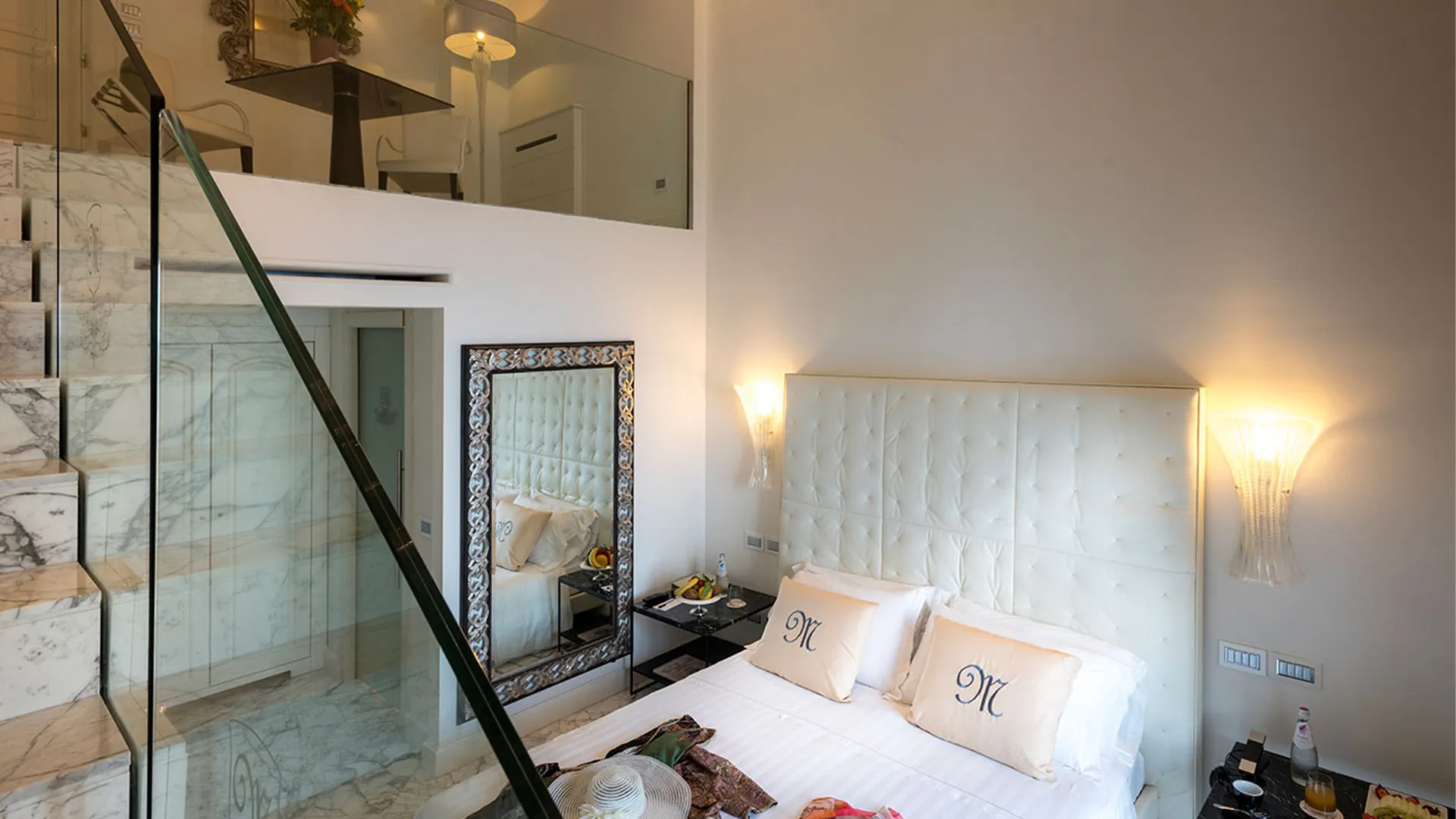 Two-level Junior Suite: marble staircase with glass railing, bed with capitonné headboard and decorative mirror