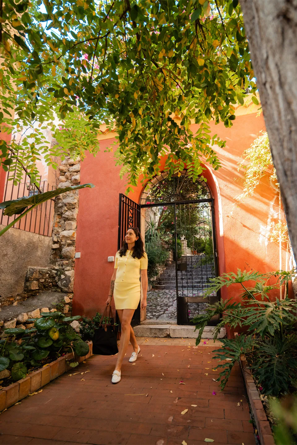 Ospite dell'Hotel Metropole passeggia nel giardino con muri in terracotta, cancello ad arco e vegetazione mediterranea