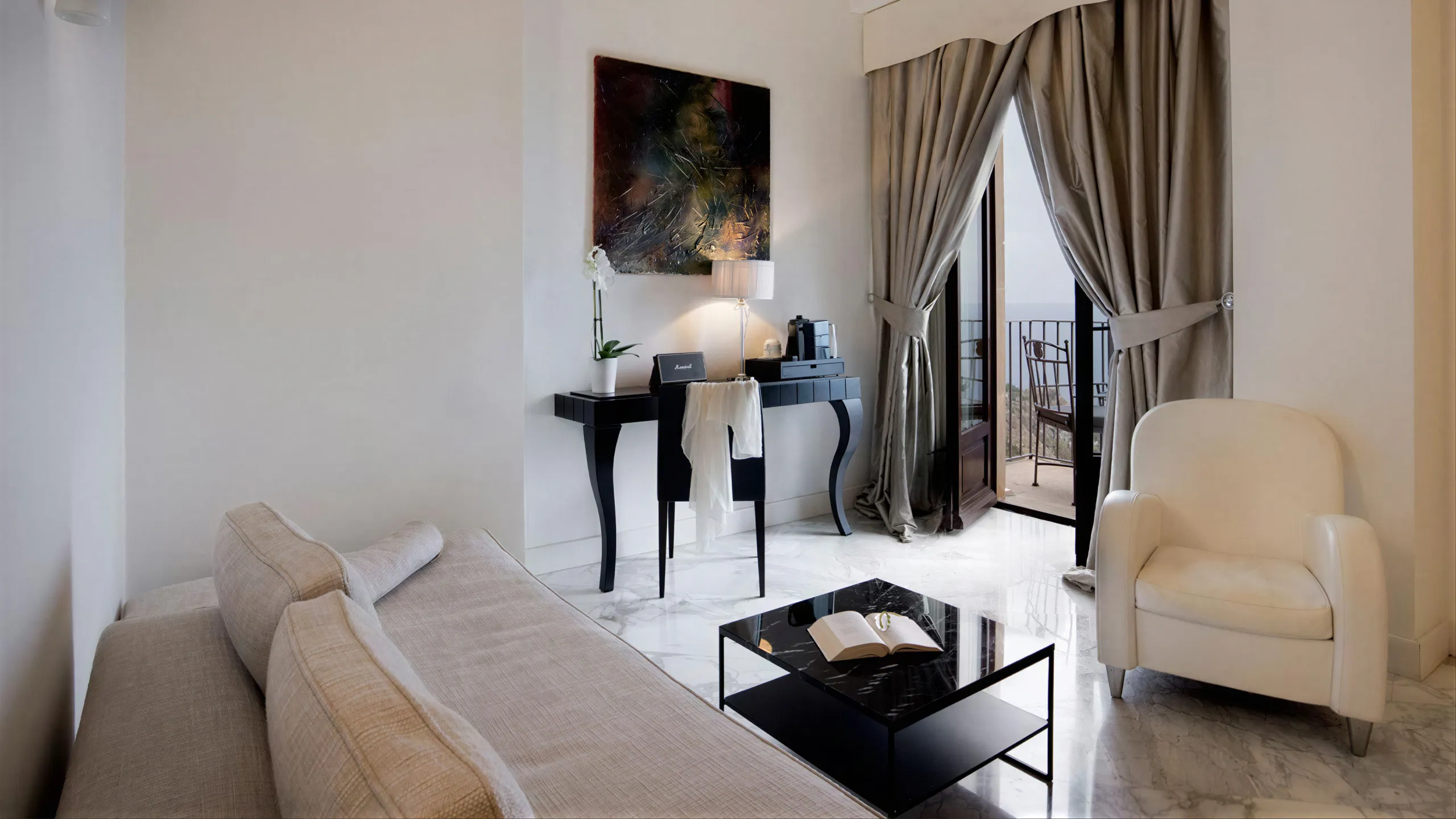 Suite vista mare: salotto con poltrona bianca, scrivania nera, speaker Marshall e porta aperta sul balcone