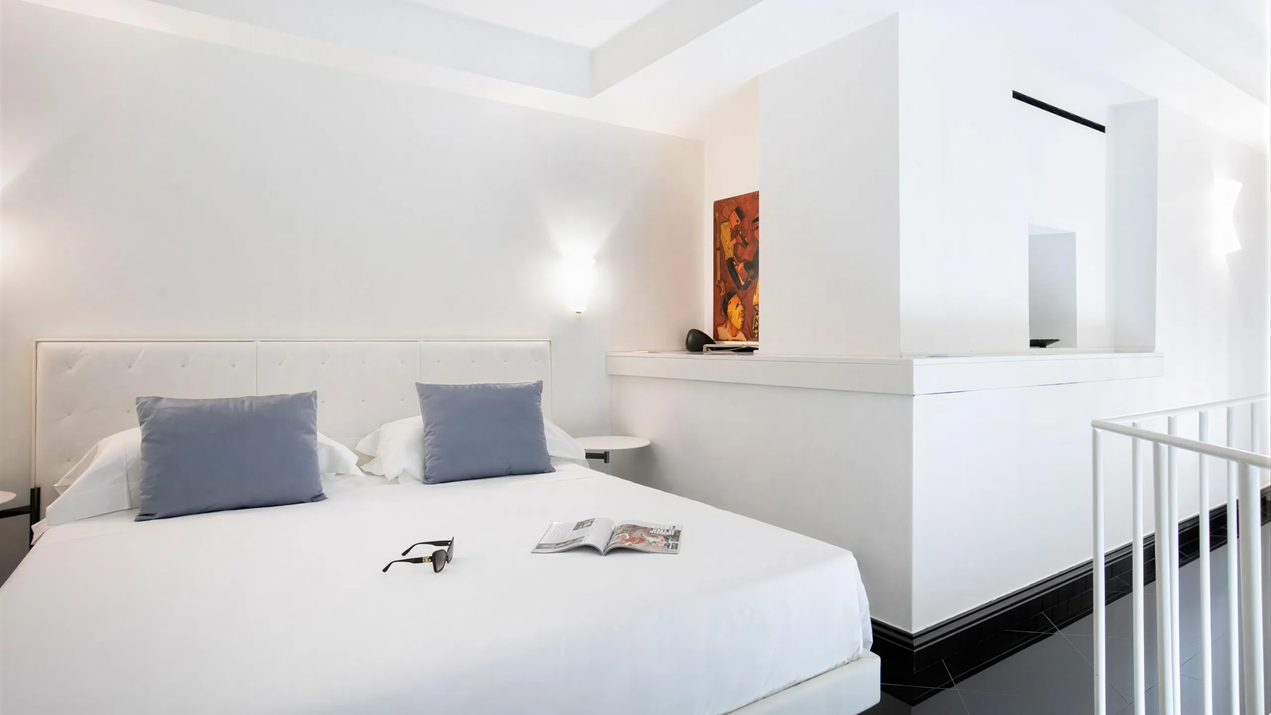 Two-level Sea View Suite: bedroom with white bed, blue pillows, artwork and white mezzanine railing